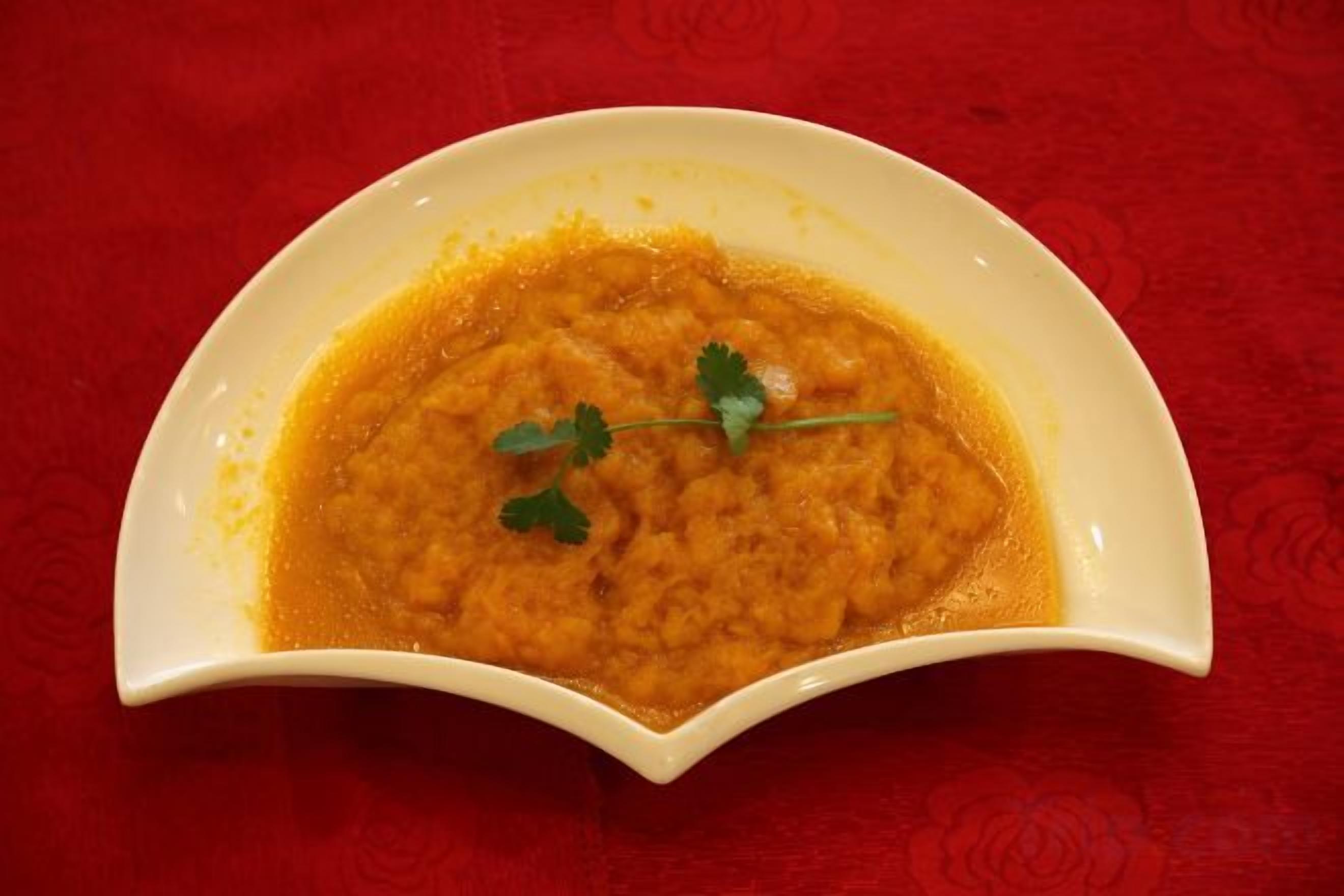 A white bowl with a textured edge containing a dish, placed on a red surface.