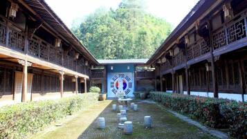 A traditional courtyard with wooden buildings, a central pathway, and a mountain backdrop.