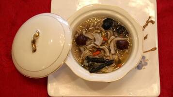 A bowl of soup with a lid on a white plate, placed on a red surface.