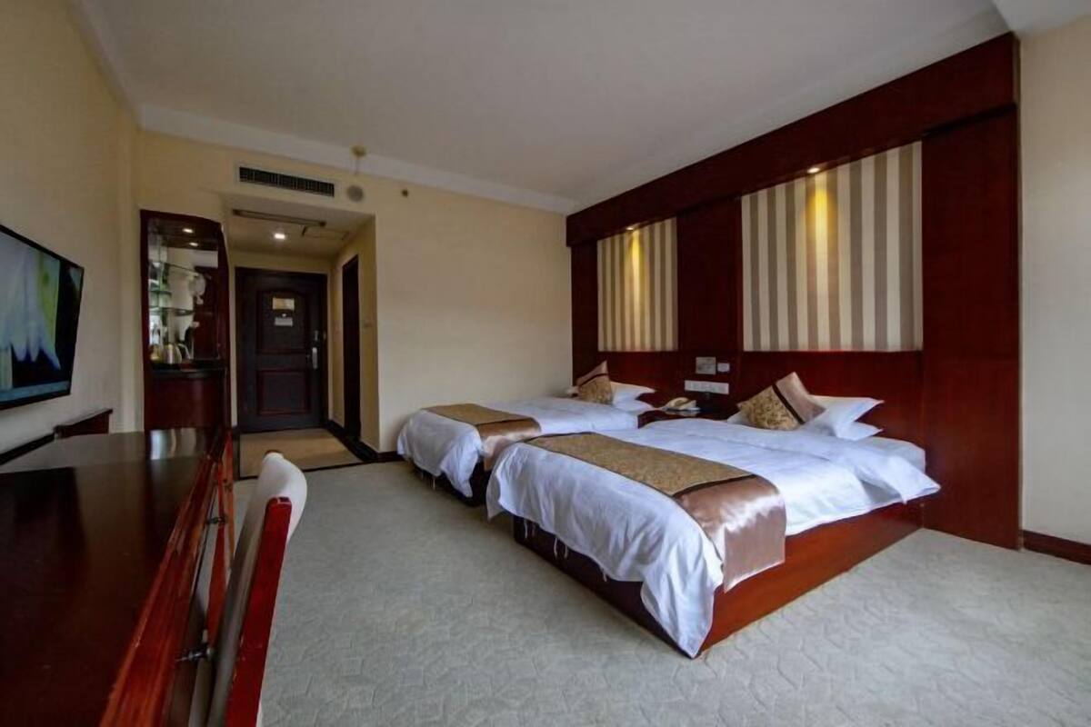 A hotel room with two beds, a desk, and a television.