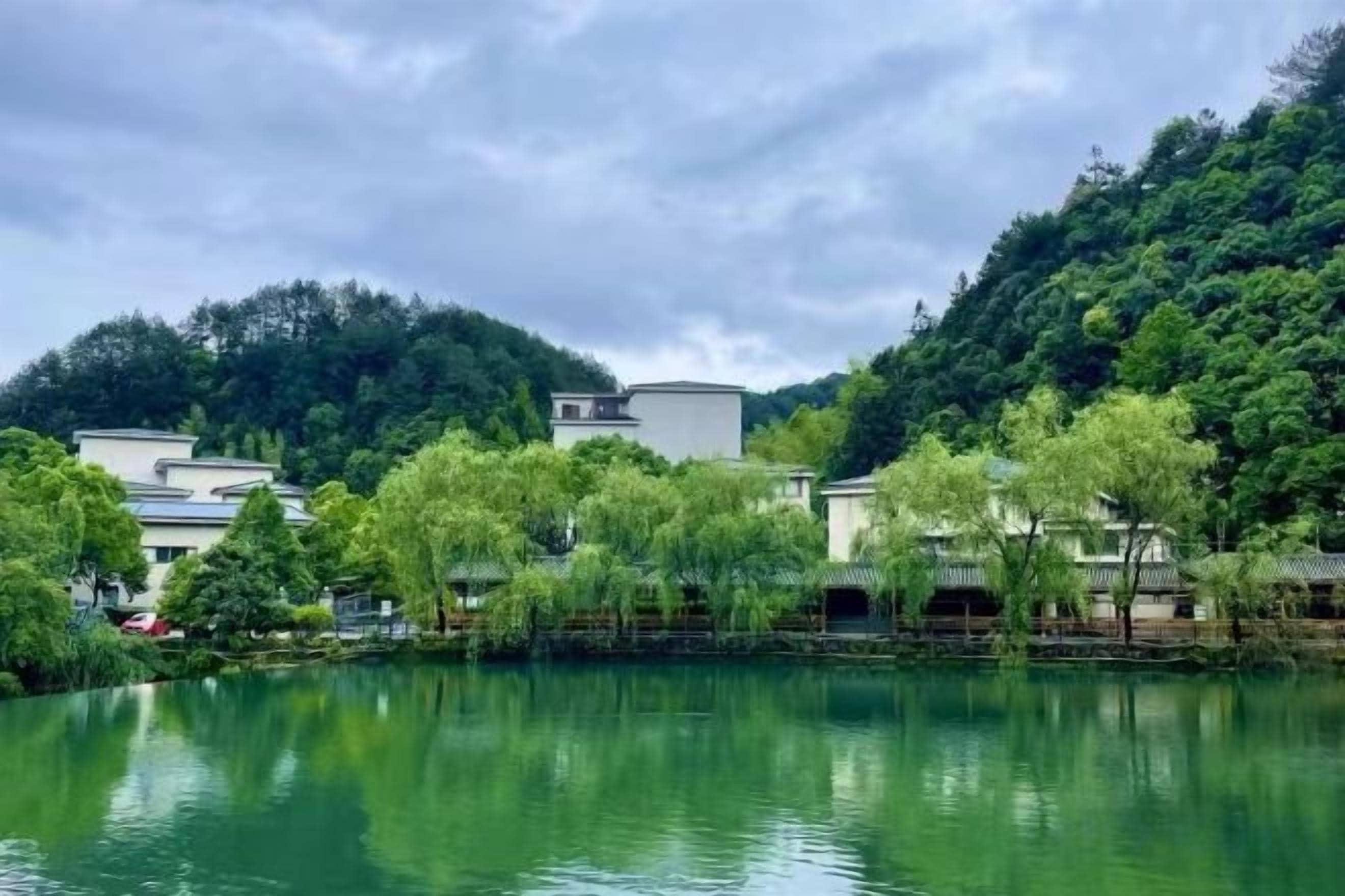 Una vista serena de un lago con edificios tradicionales y abundante vegetación.