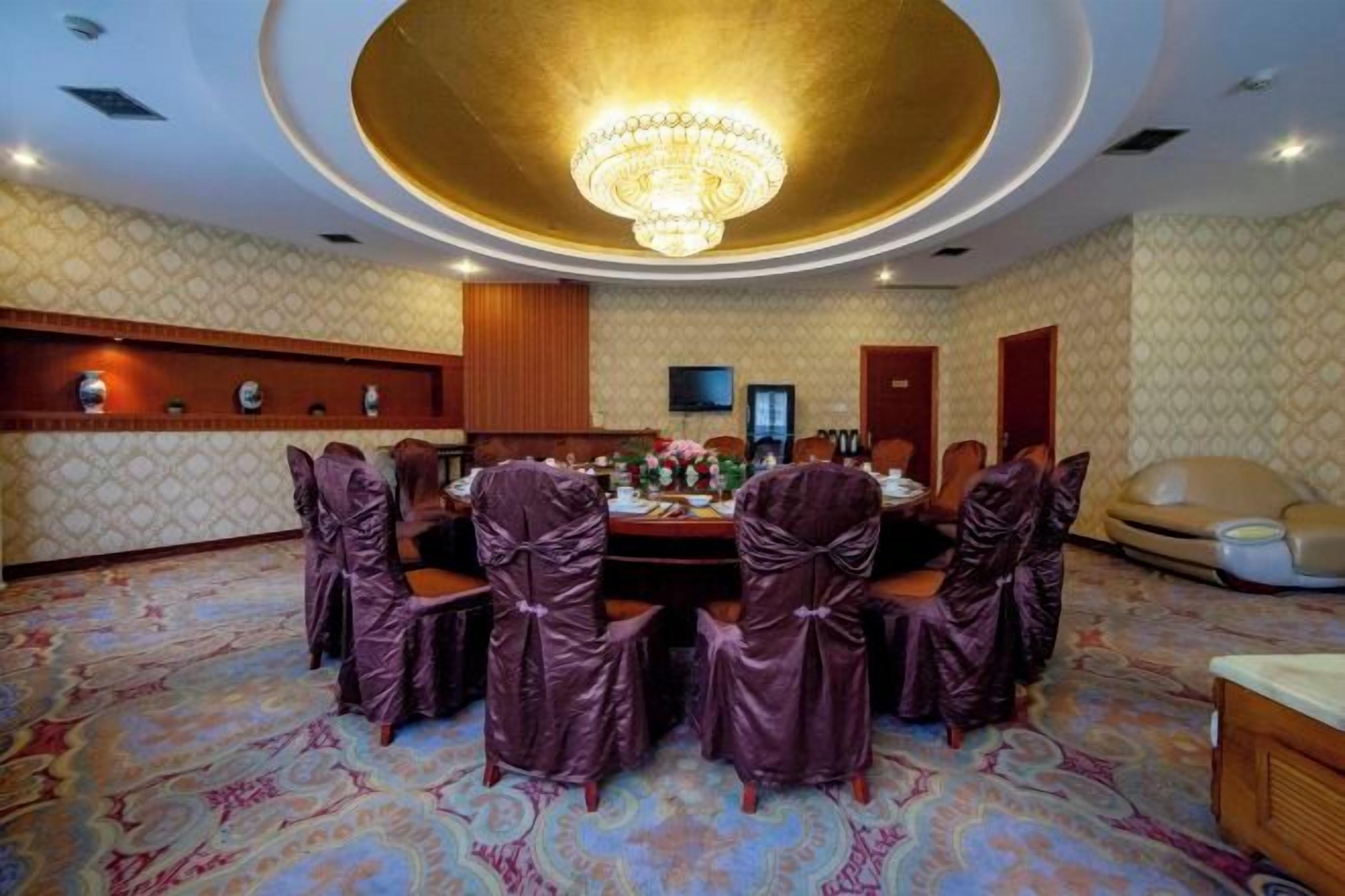 A conference room with a round table, chairs, a chandelier, and a patterned carpet.