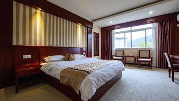 Habitación de hotel con una cama grande, cabecera de madera, una mesita y una ventana con cortinas.