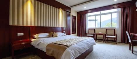 A hotel room with a large bed, a wooden headboard, a small table, and a window with curtains.
