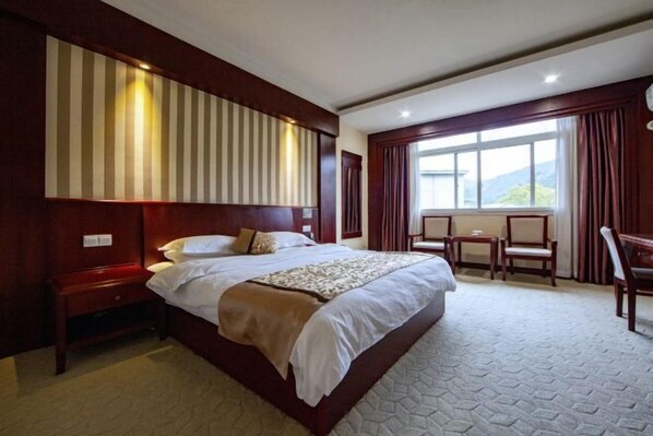 A hotel room with a large bed, a wooden headboard, a small table, and a window with curtains.