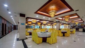 Un amplio salón de banquetes con múltiples mesas redondas cubiertas con manteles amarillos y sillas, que presenta un diseño de techo moderno con iluminación empotrada.