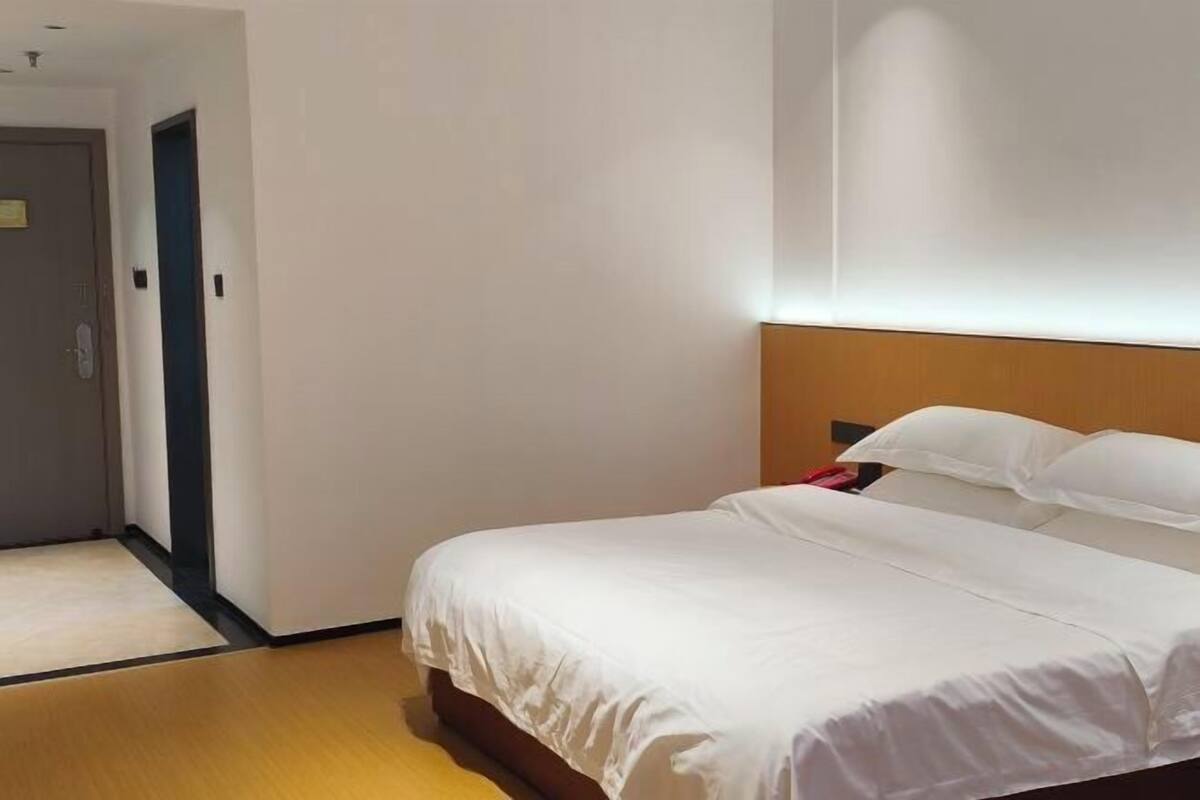 A hotel room with a bed, a wooden headboard, a door, and a light-colored floor.