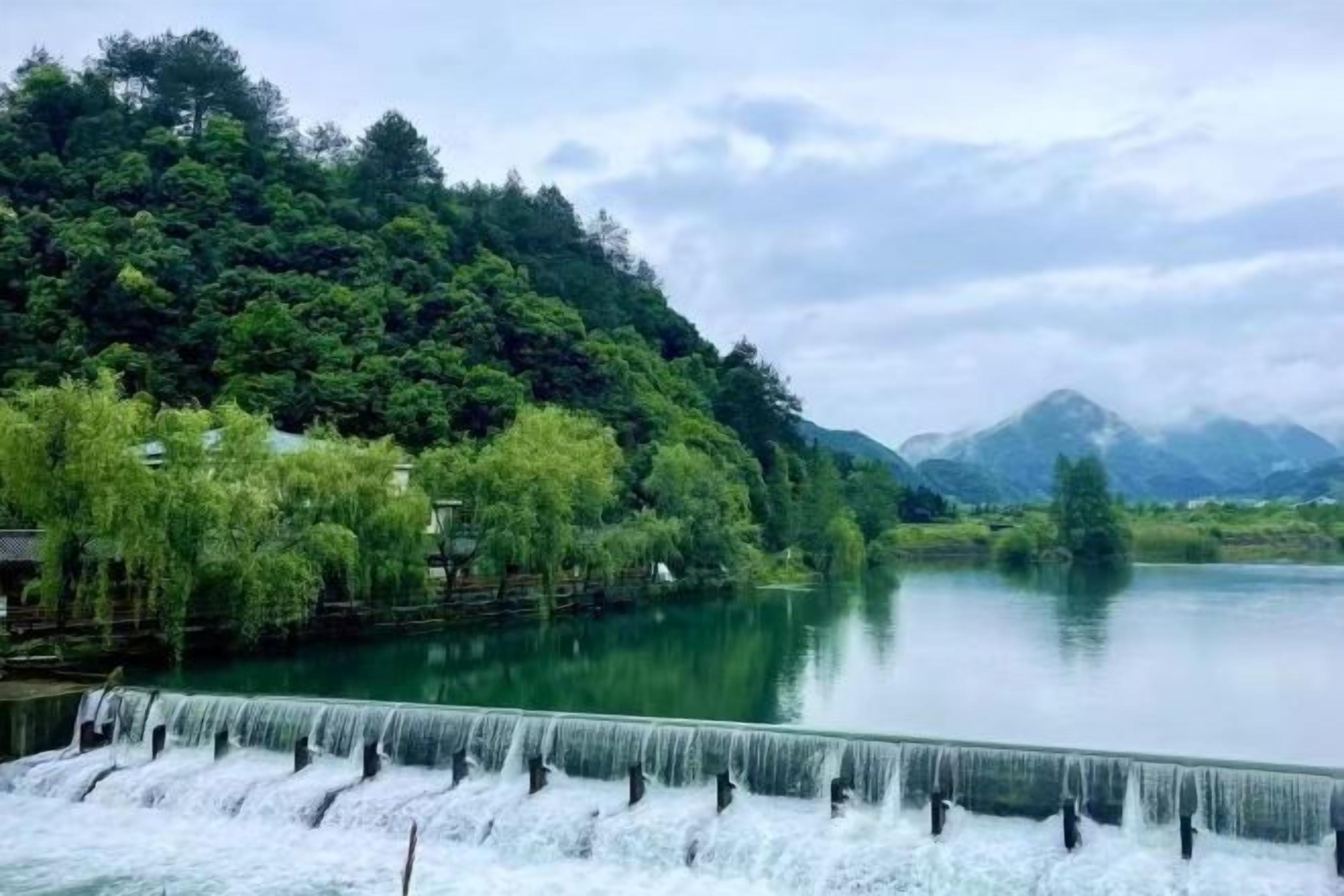 A waterfall cascading into a calm river surrounded by lush greenery and hills.