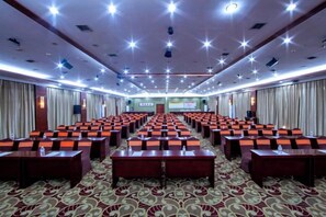 A conference room with rows of tables and chairs, a stage with a screen, and a carpeted floor. - Tianlongshan Hotel (Dexing)