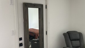 Huoneessa on valkoinen ovi, harmaa hierontatuoli ja ruskealla peitolla varustettu sänky.