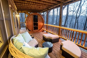 Una terraza de madera con muebles de mimbre y un ventanal grande de forma de barril.