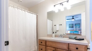 Een badkamer met een witte douchegordijn, een houten wastafel met lades, een wastafel en een spiegel.