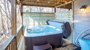 Een houten terras met een jacuzzi, een houten omheining en een stoel.