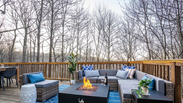 Een terras buiten met een vuurkuil, zitgedeelte en uitzicht op kale bomen.