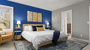 Een slaapkamer met een bed, nachtkastjes, een lamp, een stoel en een groot raam.