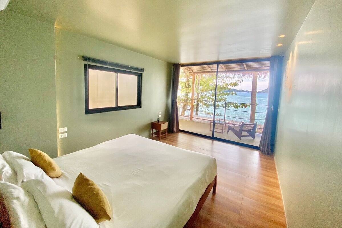 A bedroom with a large bed, a window, and a view of the sea.