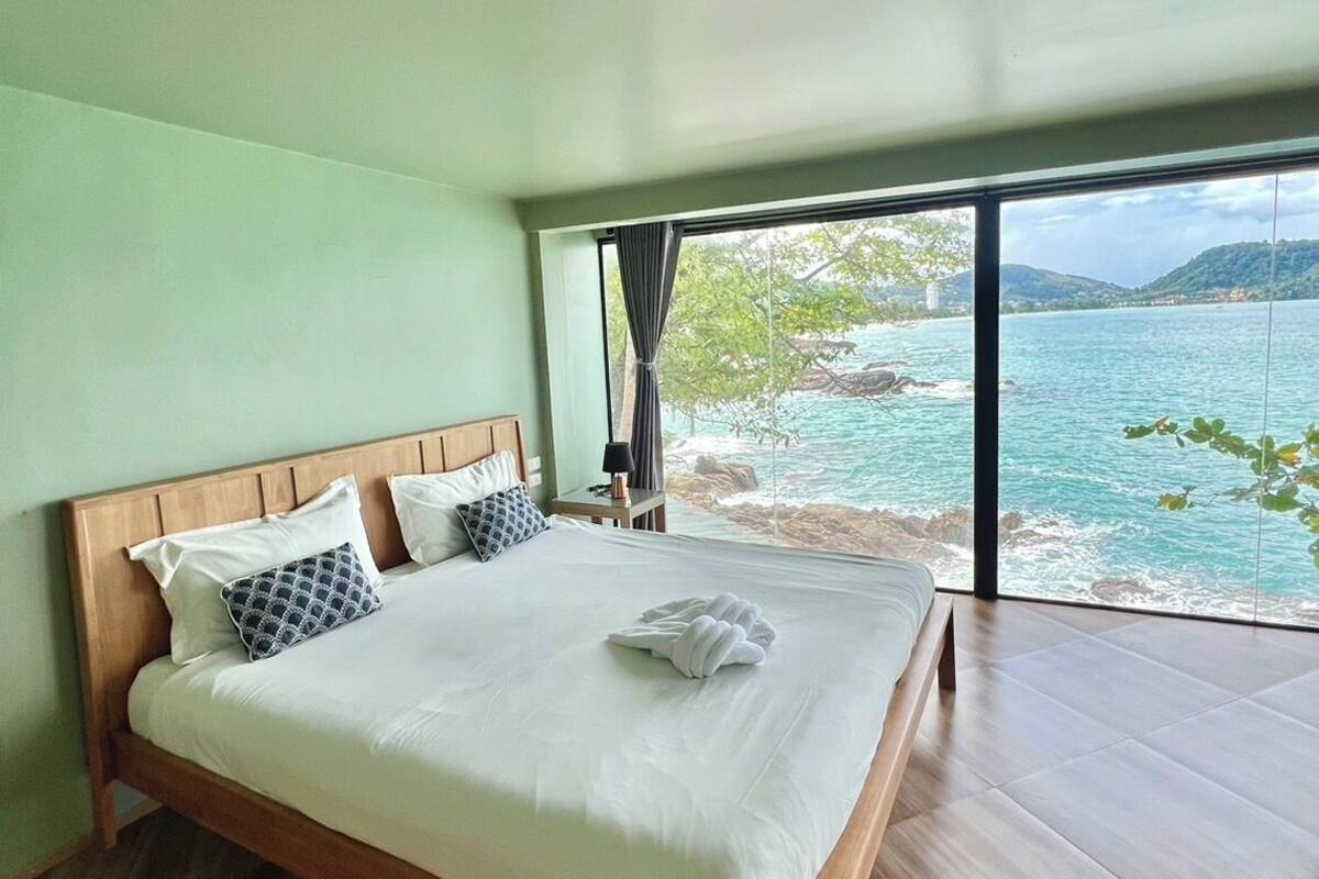 A bedroom with a large bed, wooden headboard, and a view of a body of water through large windows.