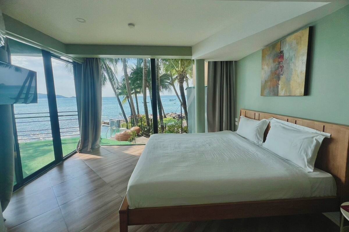 A hotel room with a large bed, a TV, and a view of the ocean.