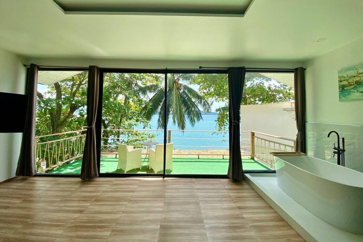 A modern room with a large sliding glass door leading to a balcony with a view of the sea.