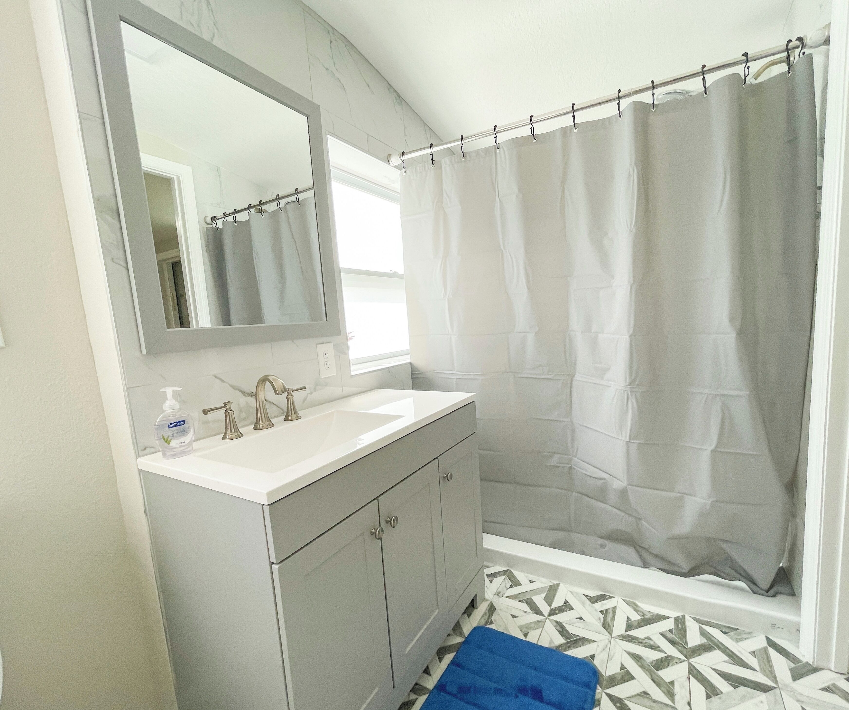 A bathroom with a white sink, a mirror, a shower curtain, and a patterned floor.