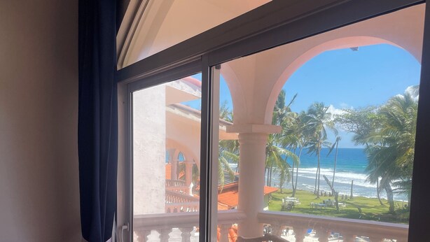 Een balkon met een witte rieten stoel en uitzicht op de oceaan, met een betegelde vloer.