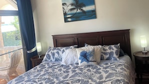 Een slaapkamer met een bed, nachtkastje, lamp, raam met gordijnen en een schilderij aan de muur.