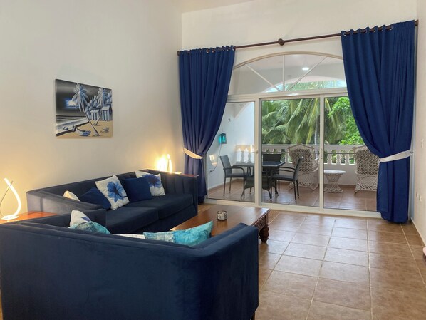 Un salon comprenant un canapé, une table et donnant sur un balcon aménagé avec du mobilier d’extérieur.