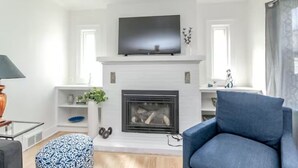 Una sala moderna con chimenea, un televisor de pantalla plana montado encima y un sillón azul.