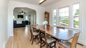 Un comedor con una mesa y sillas de madera, una araña y vistas al exterior a través de amplios ventanales.