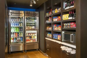 Una cuina americana equipada amb dos refrigeradors d'acer inoxidable plens de begudes i aperitius, un microones i prestatges amb aliments envasellats.