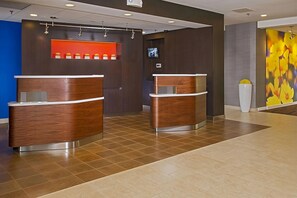 Una zona d'entrada amb dues taules de recepció de fusta, una estanteria vermella amb objectes taronja, un televisor a la paret i un gran quadre floral.