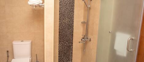 Une salle de bain comprenant des toilettes, une douche avec une porte en verre et un porte-serviettes.