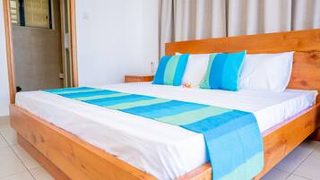 A wooden bed with white and blue bedding, a wooden nightstand, and a window with curtains.