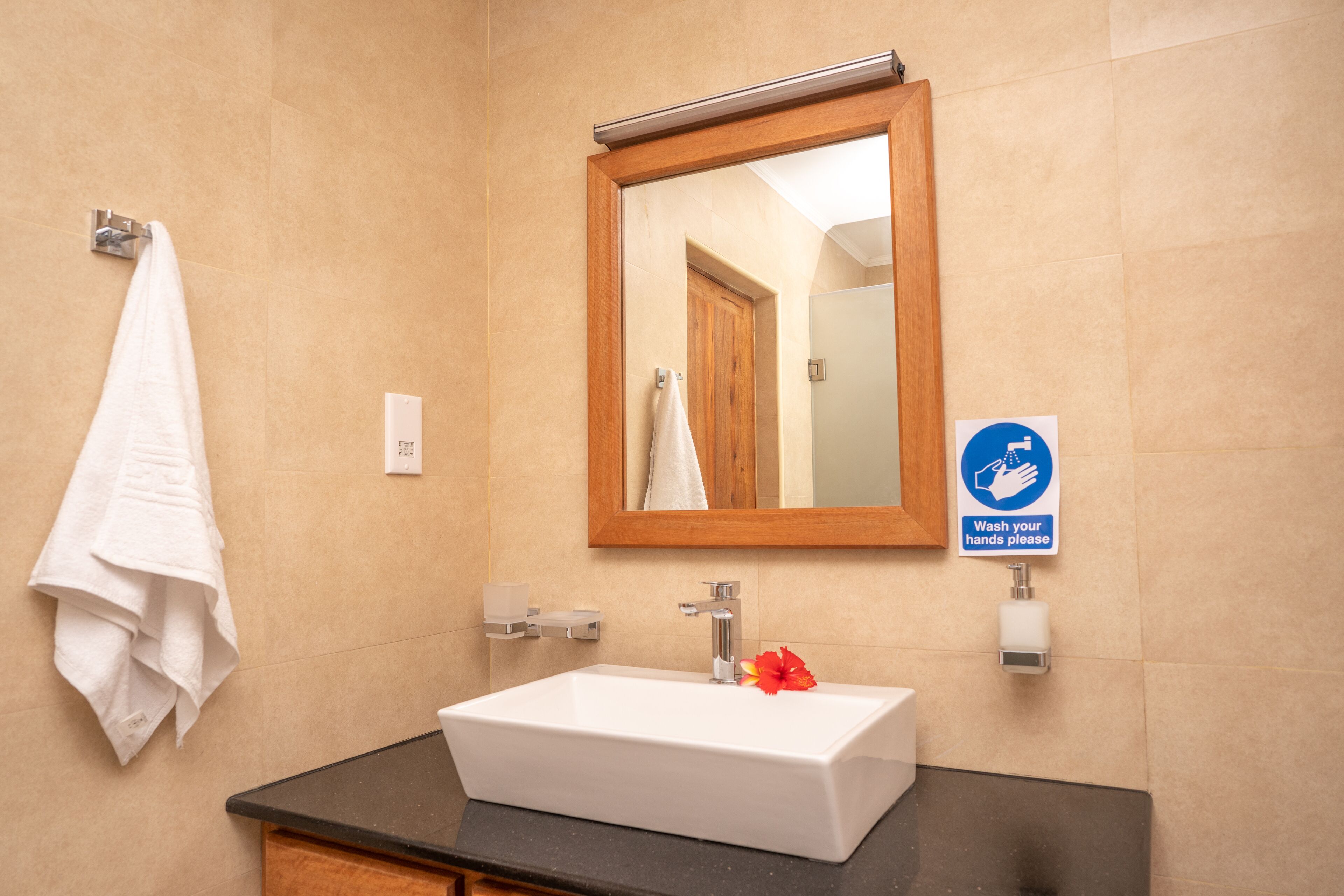 A bathroom with a white sink, a mirror, a towel rack, and a handwashing sign.