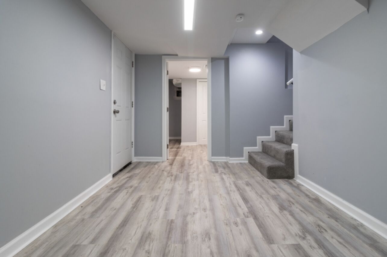 Un pasillo con paredes grises, suelo de madera y una escalera con peldaños cubiertos de moqueta gris.