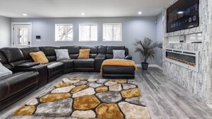 Ein modernes Wohnzimmer mit einem Ecksofa, einem Teppich mit Steinmuster und einem Flachbildfernseher, der an einer Wand mit Steinoptik befestigt ist.