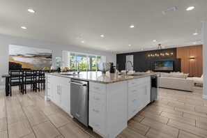 A modern kitchen with a large island, white cabinetry, and a dining area with a black table and chairs.