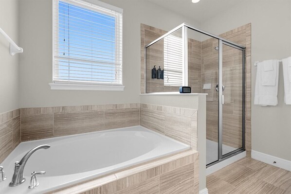 A modern bathroom with a large bathtub, a glass shower enclosure, and a window with blinds.