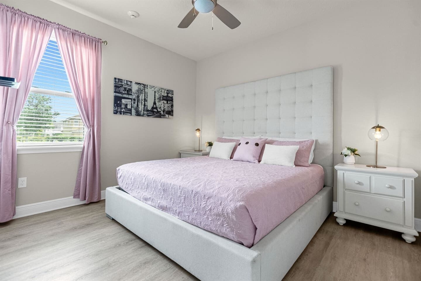 A bedroom with a bed, nightstands, a ceiling fan, and a window with curtains.