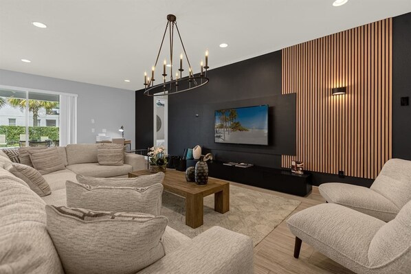A modern living room with a sectional sofa, a wooden coffee table, a TV mounted on a dark wall, and a decorative wall panel.