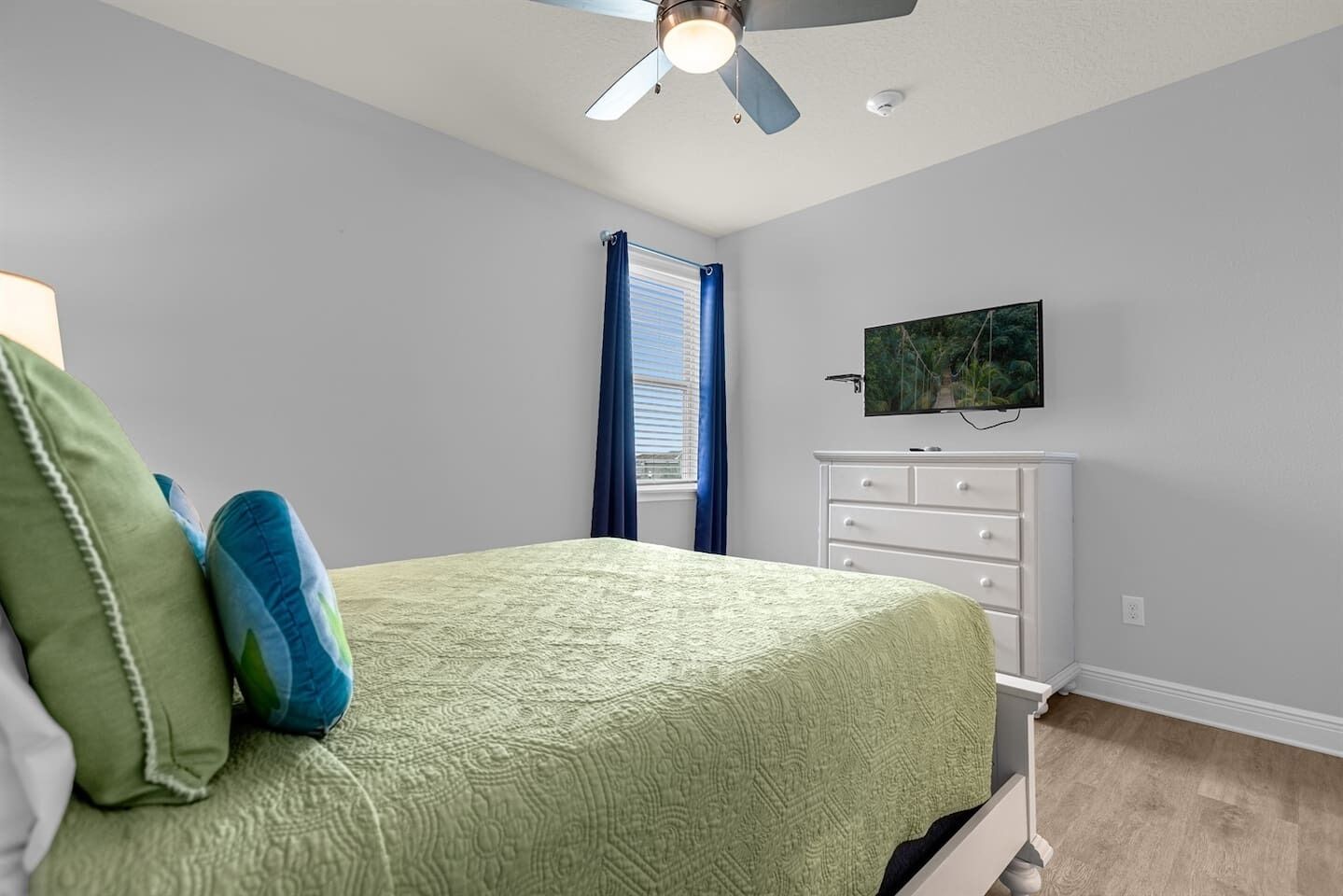 Ein Schlafzimmer mit Bett, Kommode, Deckenventilator und Fernseher an der Wand.