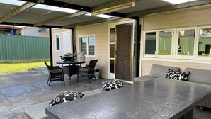Un patio exterior con una mesa de metal, sillas de mimbre y un banco acolchado.