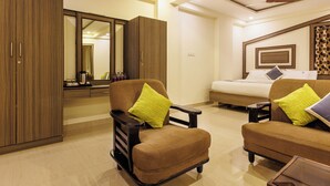 Een moderne hotelkamer met een bank, fauteuils, een bed, een kledingkast en een spiegel.