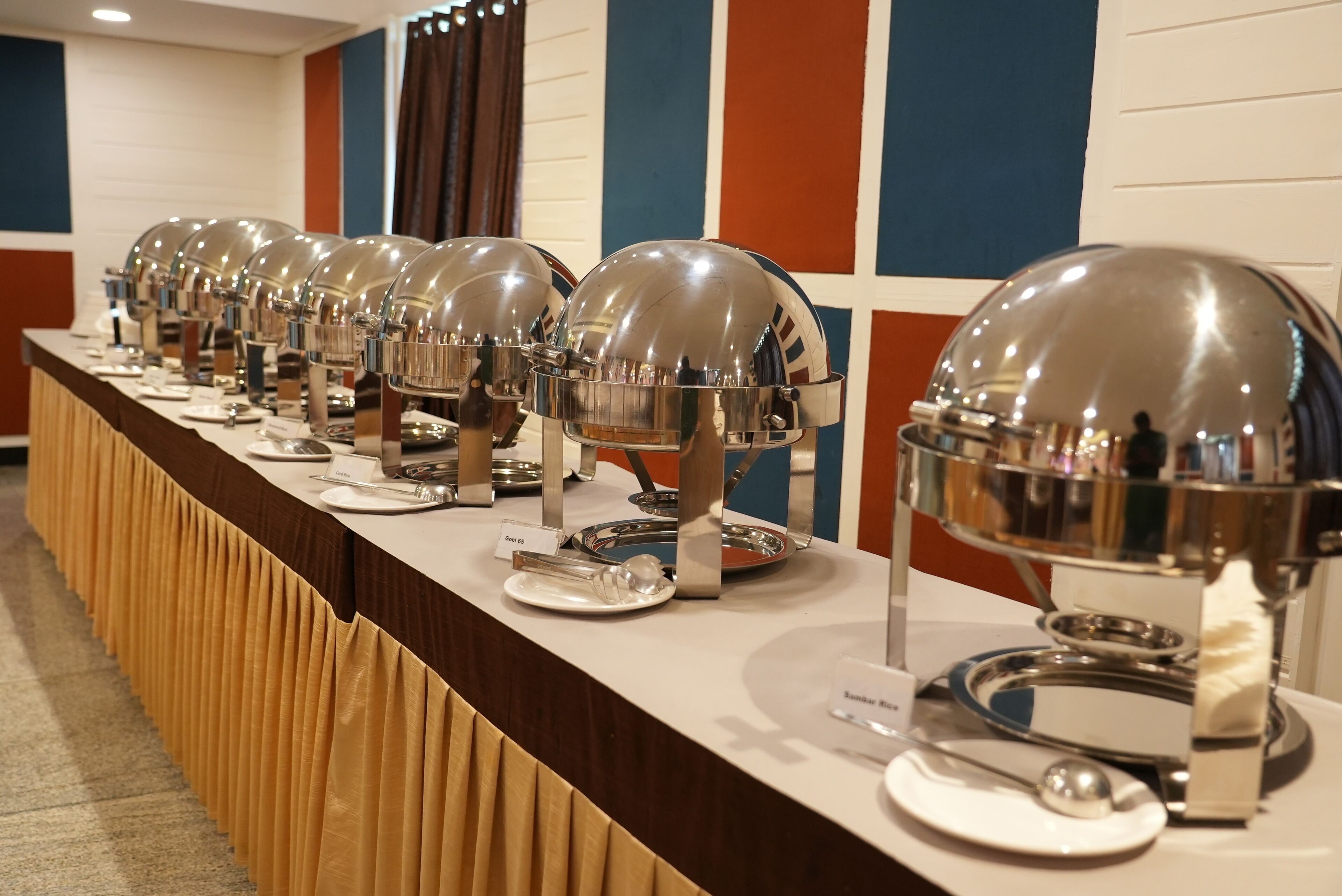 A buffet setup with multiple self-service food stations, each with a dome cover and a plate.