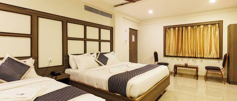 A hotel room with two beds, a ceiling fan, a bedside table, a chair, and a large window with curtains.