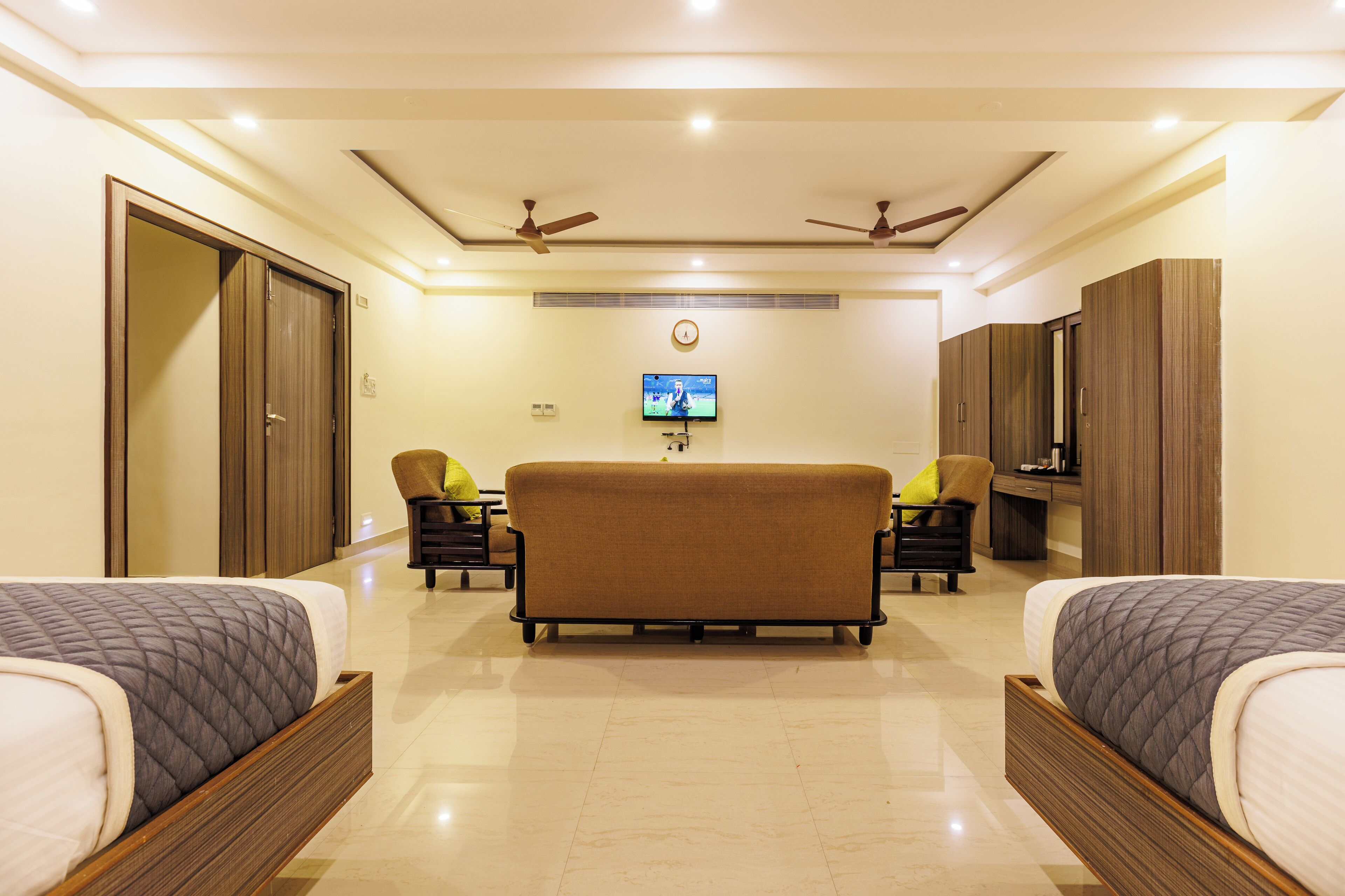A hotel room with two beds, a sofa, a TV, and ceiling fans.