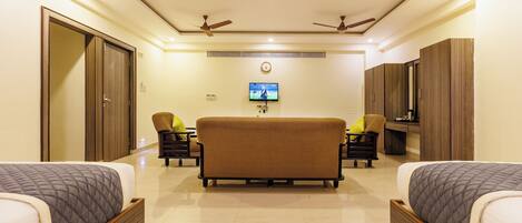 A hotel room with two beds, a sofa, a TV, and ceiling fans.