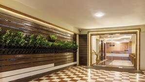 Een geruit vloertje, een houten bankje en een muur met planten.