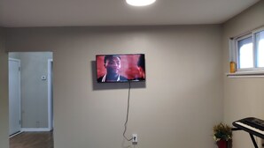 A living room with a flat-screen TV mounted on the wall, a potted plant, and a keyboard on a stand. - Comfortable 3BD home -5 mins to Scarborough Town center (Toronto)