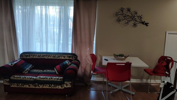 A living room with a patterned sofa, a dining table with chairs, and a decorative wall piece. - Comfortable 3BD home -5 mins to Scarborough Town center (Toronto)